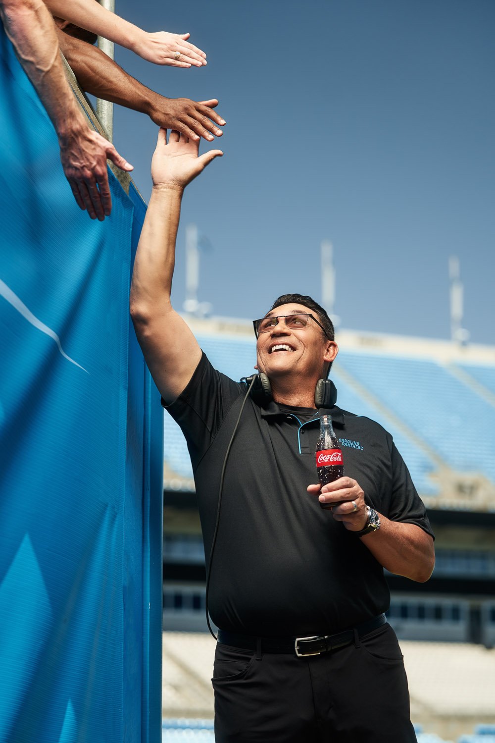 A Carolina Panther's coach giving high-fives to fans while holding a Coca-Cola