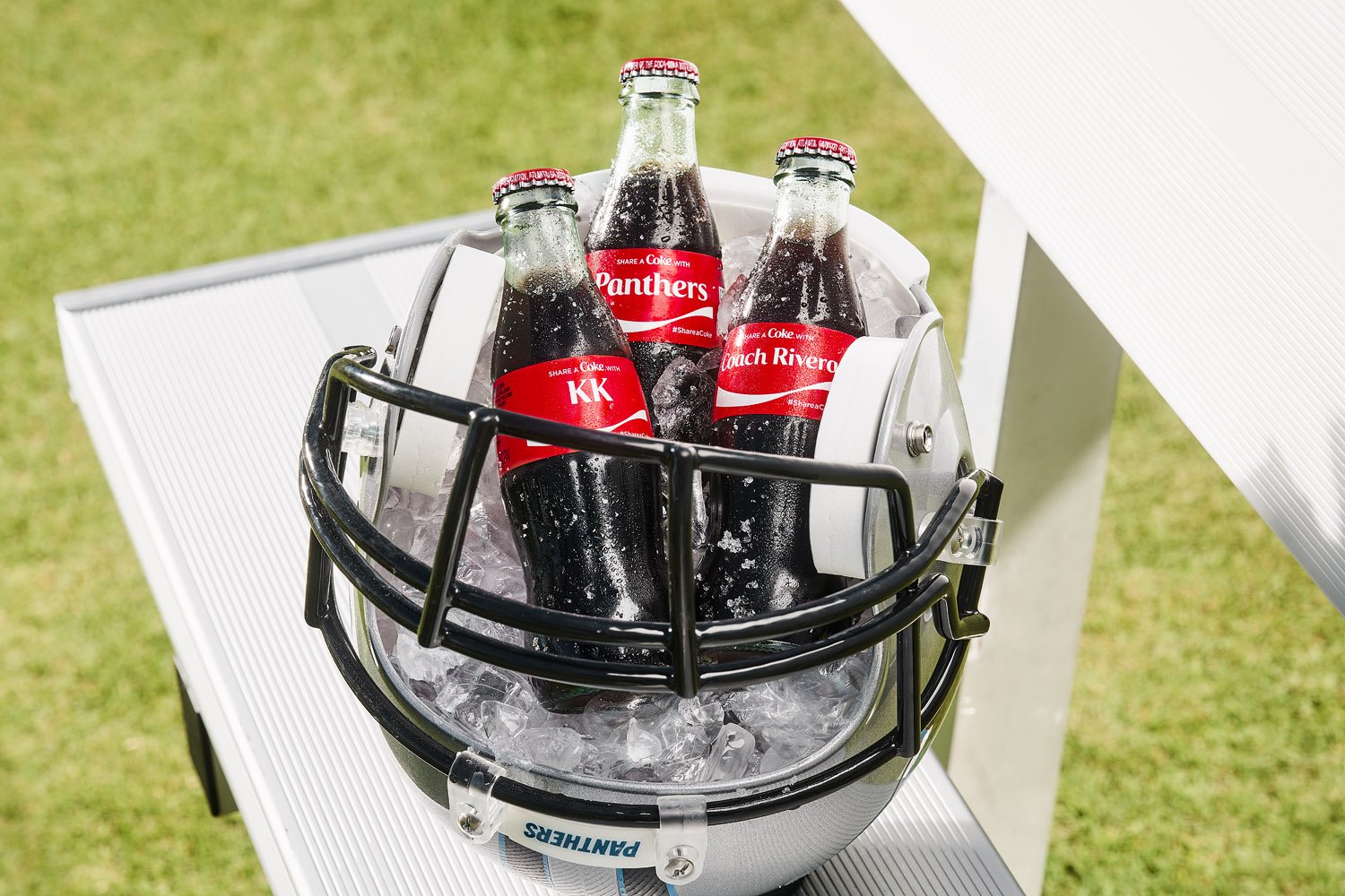 Still life product photo of three glass Coca-Cola bottles inside of an upside down football helmet filled with ice