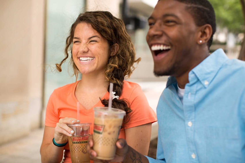 Photographer Liz Nemeth's photo for Krispy Kreme's social media campaign. The photo features two people drinking cold coffee drinks from clear Krispy Kreme plastic cups. On the left is a white woman wearing a coral t-shirt and on the left is a black man wearing a light blue button-down shirt.