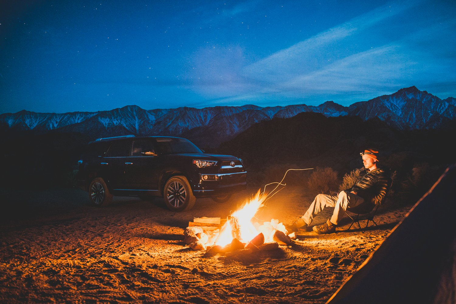 Toyota 4Runner and a camper pictured next to a cozy fire in a mountainous region, photo by Mark Skovorodko.