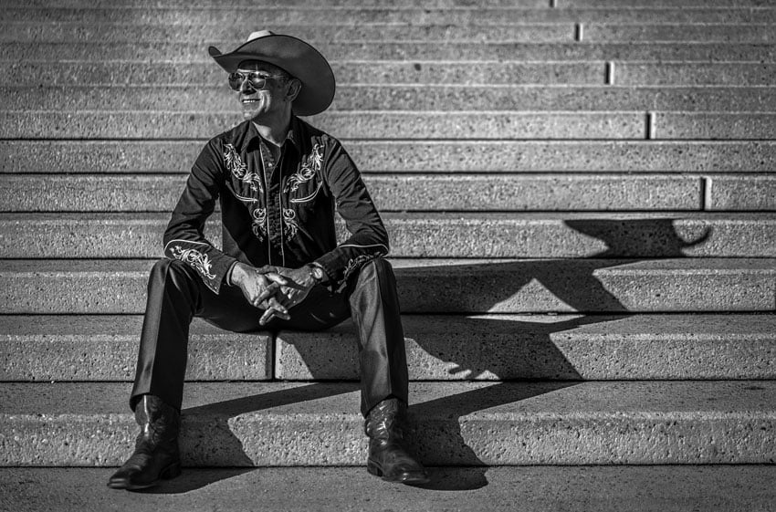 Portrait of a man in a cowboy hat and shirt sitting on the stairs, shot by Michael Schoenfeld.