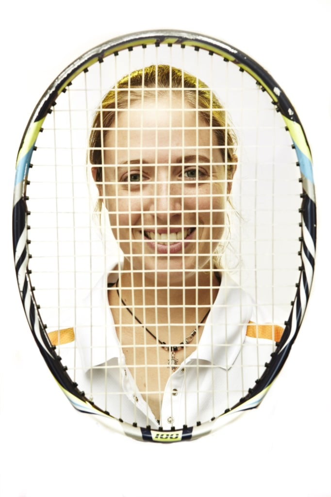 Photo of a tennis player smiling from behind her racket.