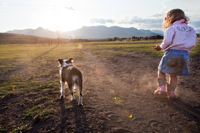 Portrait of a little girl with mud on the back of her skirt, walking her dog through a field in Montana