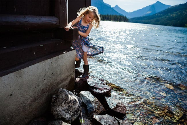 Image of a young girl in a blue dress and rainboots, playing by the water on "the rez" during a sunny day