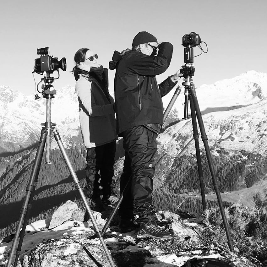 A photo of the photographic duo Scanderbeg Sauer at work. They are dressed warmly and there are snowy mountains in the background.