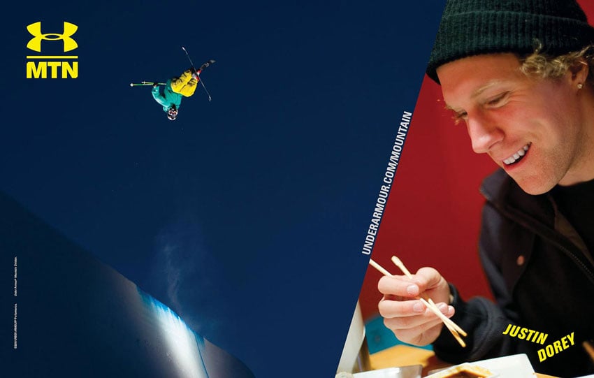 A tear sheet for Under Armour by Scott Markewitz featuring two photos of Justin Dorey, Canadian freestyle skier. On the left, Justin is airborne and upside down in his skis. He wears a teal jacket and yellow pants, a helmet, and goggles. On the right is a photo of him wearing a black beanie and black jacket. He is smiling and holding a pair of chopsticks poised over some food, which is not in the frame.