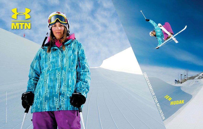 A tear sheet for Under Armour by Scott Markewitz featuring two photos of Jen Hudak, American freestyle skier. On the left is a portrait of Jen standing with her ski poles in each hand. She wears a teal jacket with an interesting dotted print, purple pants, and a hot pink layer under her jacket. She also wears a helmet and ski goggles that are pulled away from her eyes and rest above her eyebrows. On the right is a photo of Jen skiing. She is airborne and her white skis are crossed in an X-shape. 