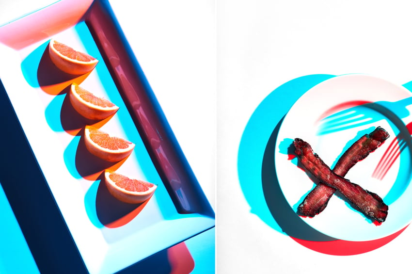 A diptych of photos by photographer Shea Evans. On the left is a photo of a rectangular dish containing 4 identical half moon shaped orange or grapefruit slices in a row. The objects all cast teal shadows and pinkish orange shadows. On the right is a photo of a round white dish with two pieces of crispy bacon forming an X on it. A dual shadow of a fork can be seen on the plate. The objects all cast a teal shadow and a red shadow.