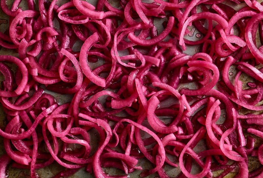 An image captured by photographer Stephen DeVries of pickled slices of red onion spread out on a cookie sheet.