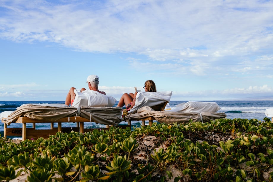 Creative in Place: Be My Guest photographer Ian Tuttle's photo of a couple lounging on reclined beach chairs on a deck looking out over the ocean. There are interesting succulent beach plants in the foreground.