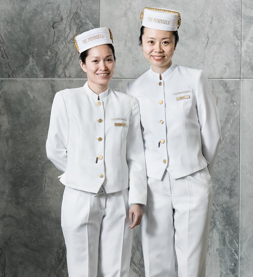 An image by Creative in Place: Be My Guest photographer George Kamper. The photo features two women in white bellhop uniforms with gold buttons. Their hats say "THE PENINSULA."