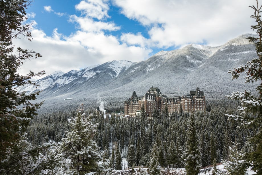 Creative in Place: Be My Guest photographer Tegra Stone Nuess' photo of a grand looking hotel nestled into a snowy evergreen forest on the side of a mountain.
