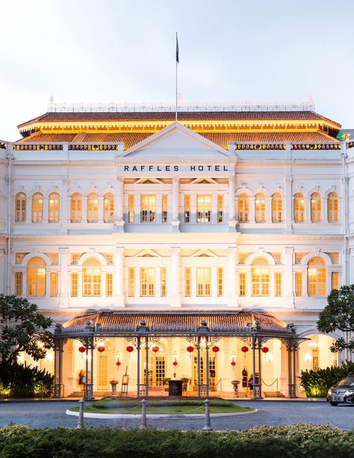 Lauryn Ishak's photo of the grand-looking Raffles Hotel in Singapore. It is dusk and the hotel is lit up, and there are red paper lanterns hung around the portico.