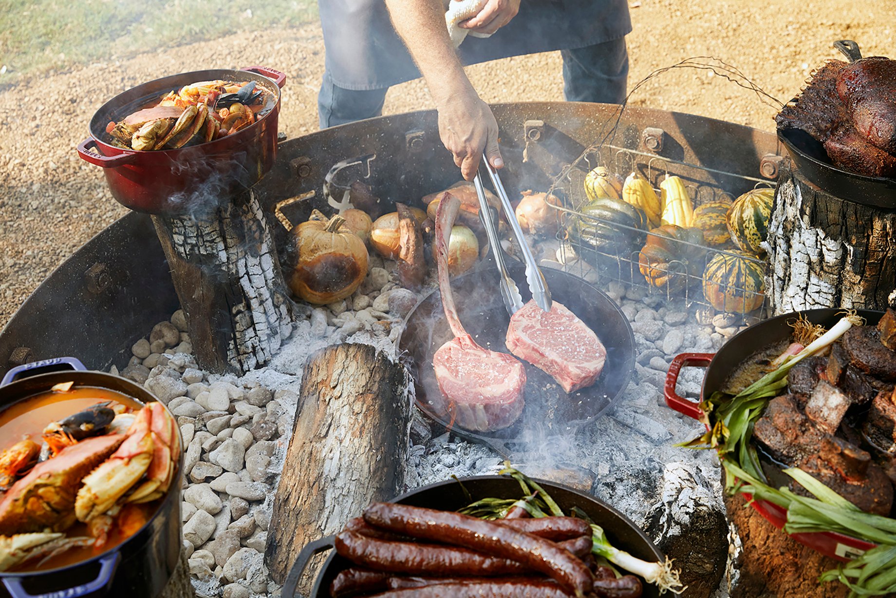 Array of meats and vegetables roasting in a large charcoal pit shot by Buff Strickland on Driftwood Ranch