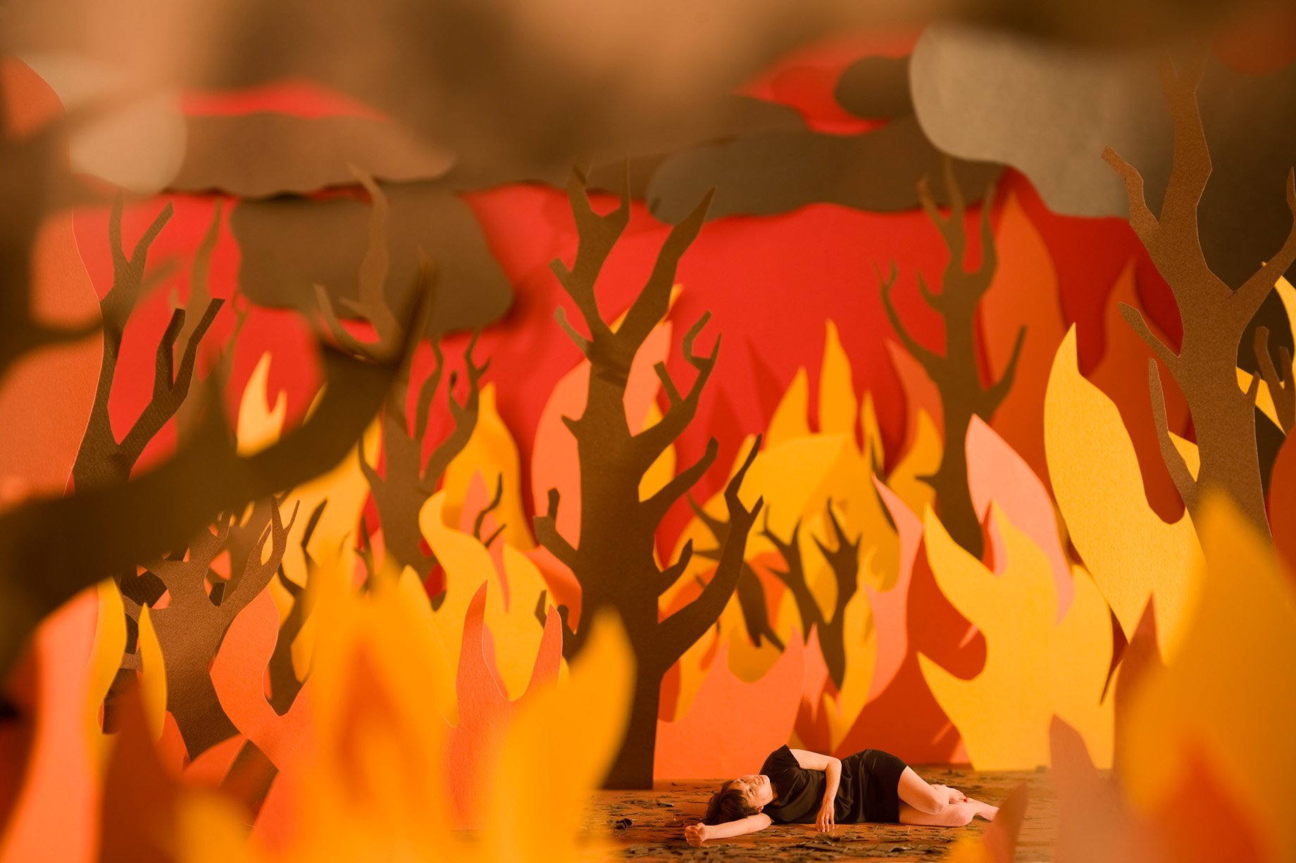 Woman lying amid wildfires constructed from color paper shot by Patrick Heageny for Paper Thin