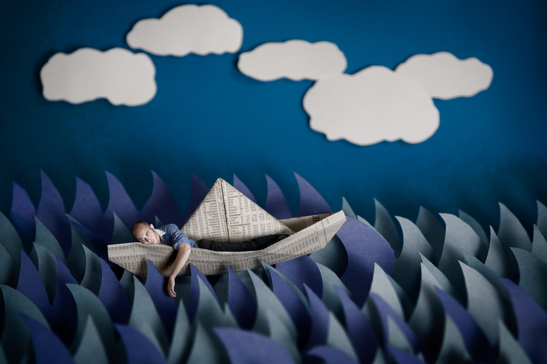 Man sits in newspaper boat made from construction paper shot by Patrick Heageny for Paper Thin
