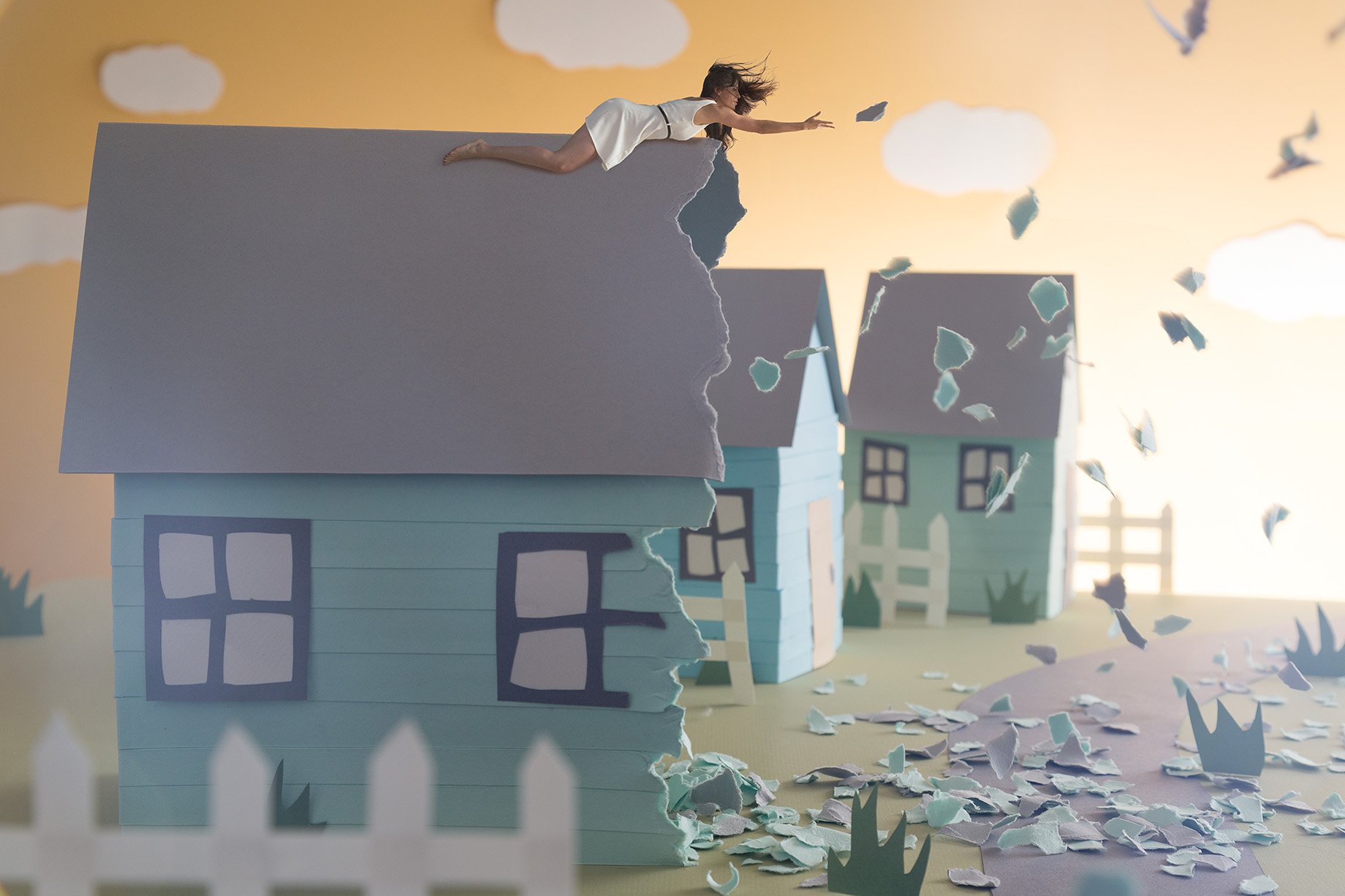 Woman on roof reaches out as house tears away made from construction paper shot by Patrick Heageny for Paper Thin