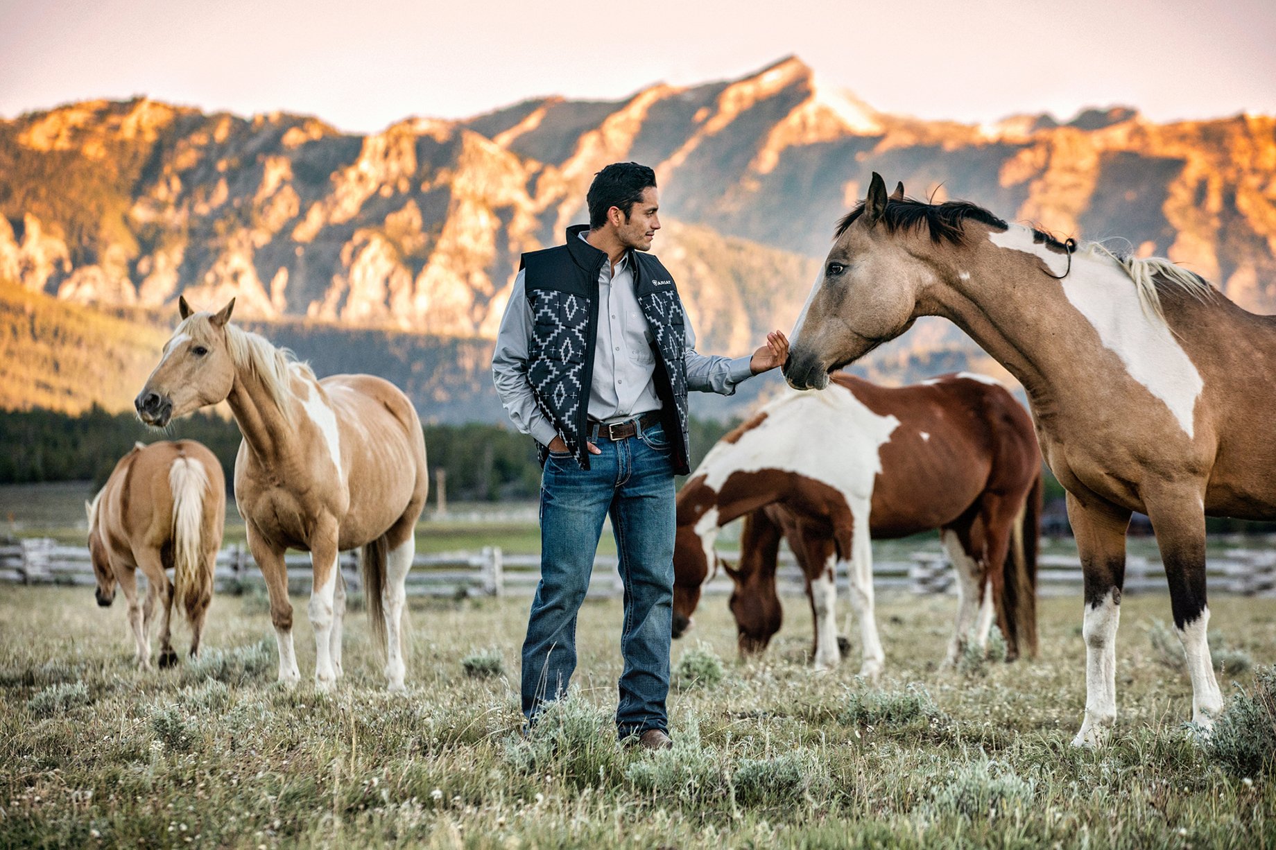 Man pets horses in pasture shot by Hillary Maybery for Ariat
