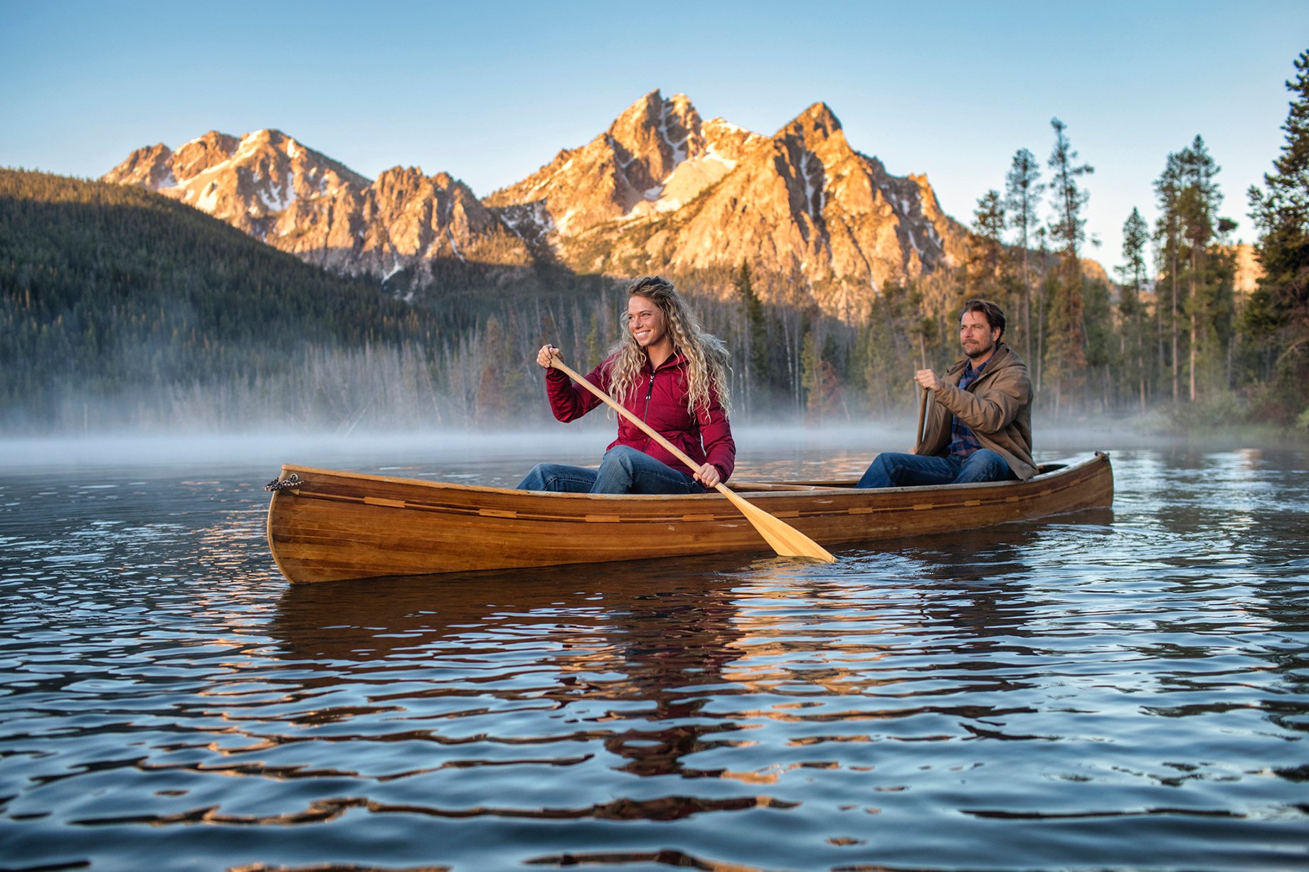 Woman and man canoe on a foggy lake with sunlit mountains behind shot by Hillary Maybery for Ariat