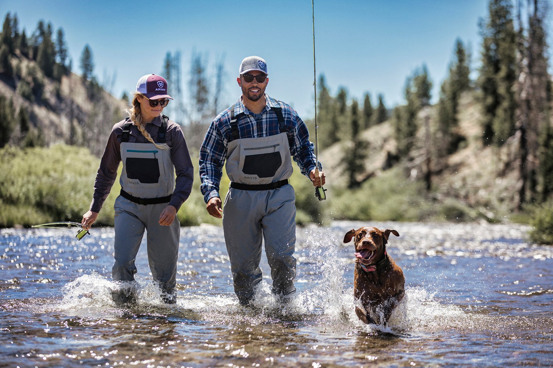 Woman and Man trek up a rive with fishing gear and dog shot by Hillary Maybery for Ariat