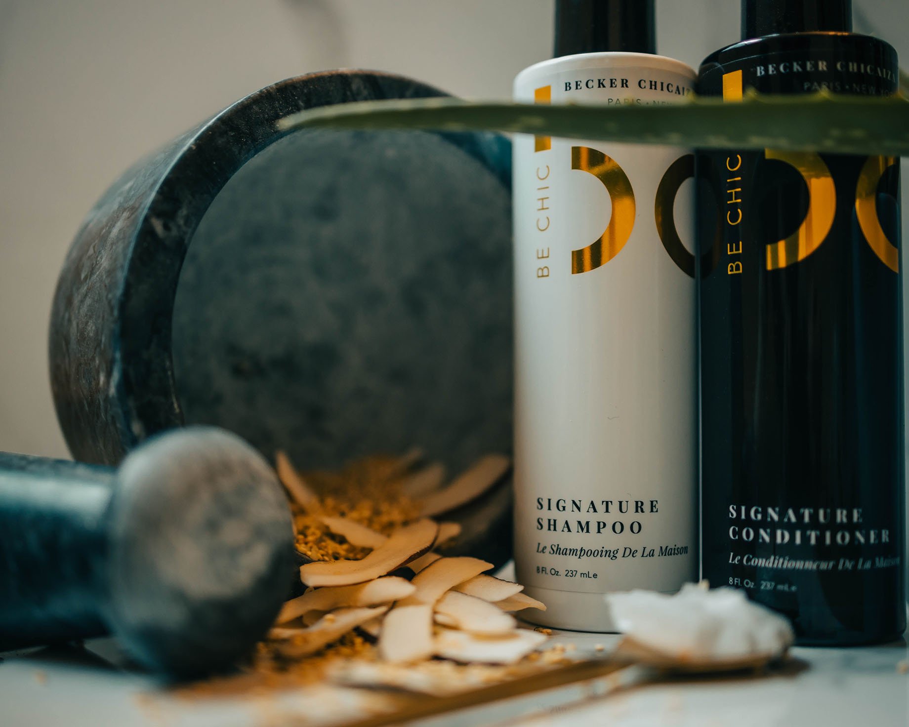 Be Chic's Signature Shampoo and Conditioner next to a mortar and pestle with coconut oil and flakes shot by Chad Savage