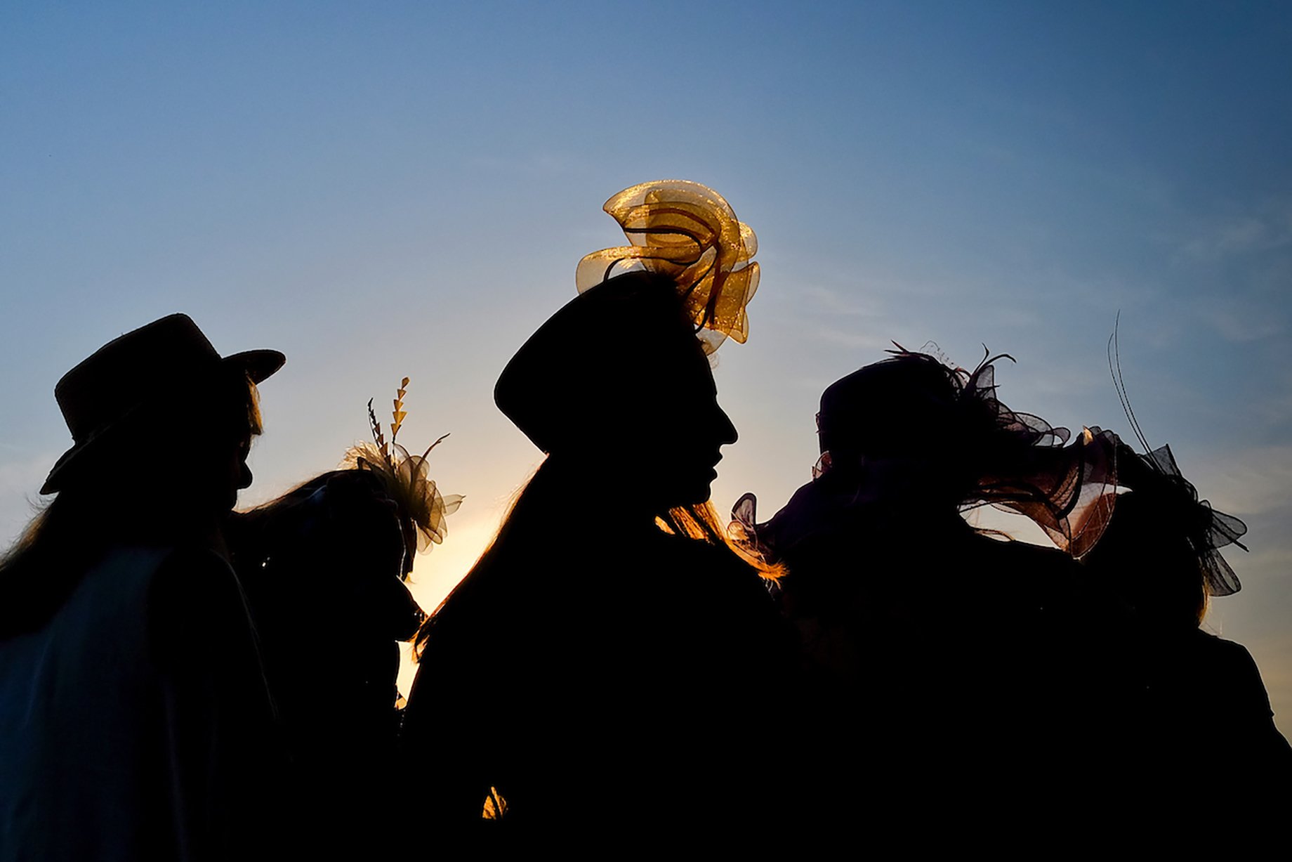 Women with fluffy hats silhouetted in front of a sunset at Churchill Downs shot by William DeShazer
