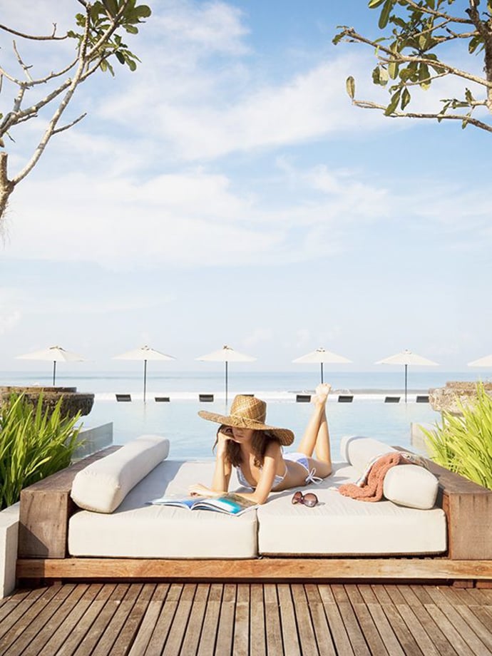 Photographer Lauryn Ishak's photo of a woman in a bikini and a wide brimmed hat lounging on a pool deck on a day bed while looking at a magazine. Straight across the background is a line of white beach umbrellas.