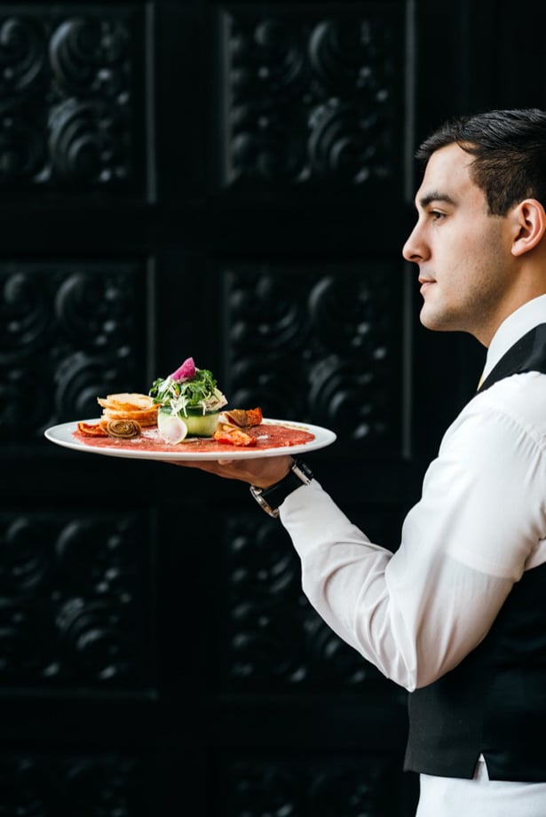 John Davidson's image of a waiter in profile holding a charcuterie platter on a white dish.