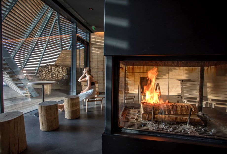 Photographer Cristina Candel's image of a woman in a stylish lounge with a central fireplace. She gazes out the window.