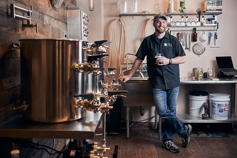 Brewer Greg W. holding a glass of beer in his brewing area. Photographed by CJ Foeckler. 