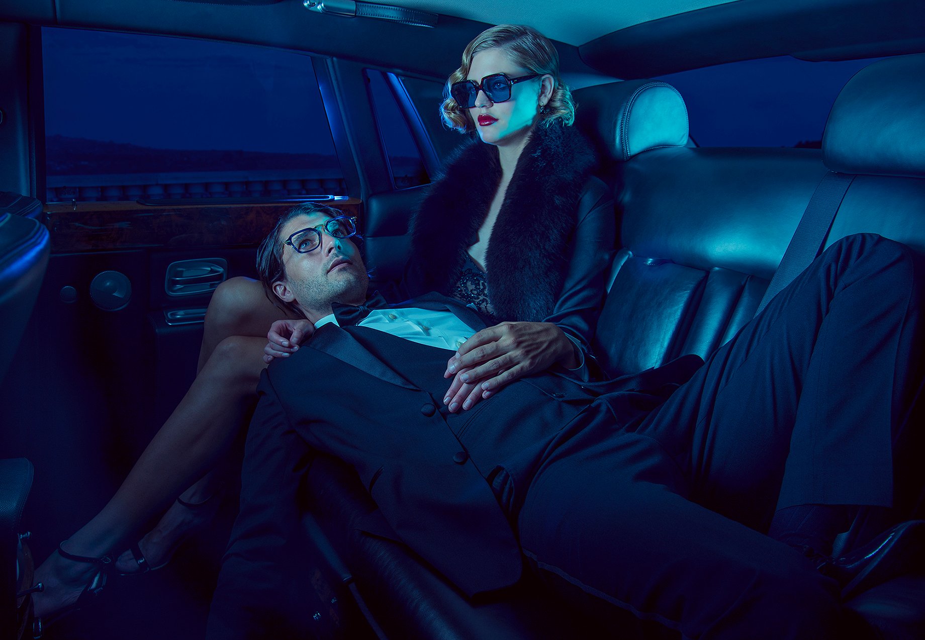 Man in glasses lays on lap of woman with sunglasses in the back of a dark limousine shot by Greg Miles for Dita Eyewear