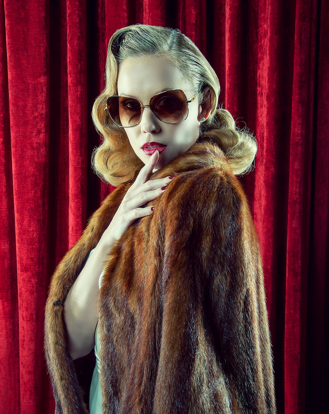 Woman in sunglasses, red lipstick, and fur coat in front of red velvet backdrop shot by Greg Miles for Dita Eyewear