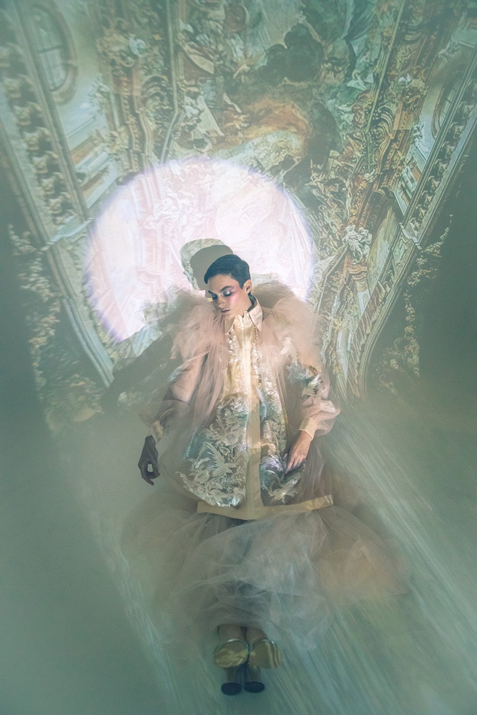 Model Amelia Pool wearing silver and gold flower embellished coat sitting in front projected Renaissance art shot by Kirsten Miccoli