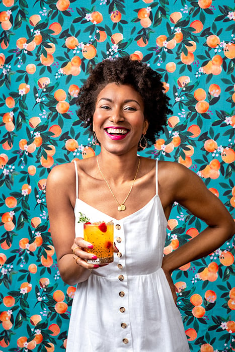 A playful portrait of a woman holding a Clementine Skies. The clementine backdrop and model's matching pink lipstick and nails add pops of color throughout the image. 