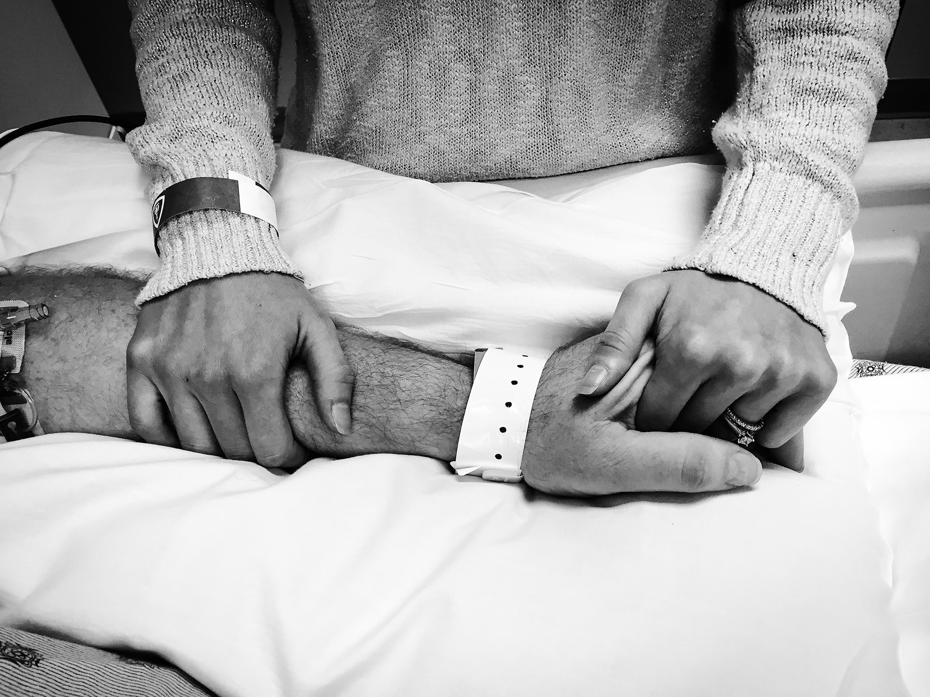 Photographer Sean Scheidt's sister holding their Uncle's hand in a hospital bed shot in black and white