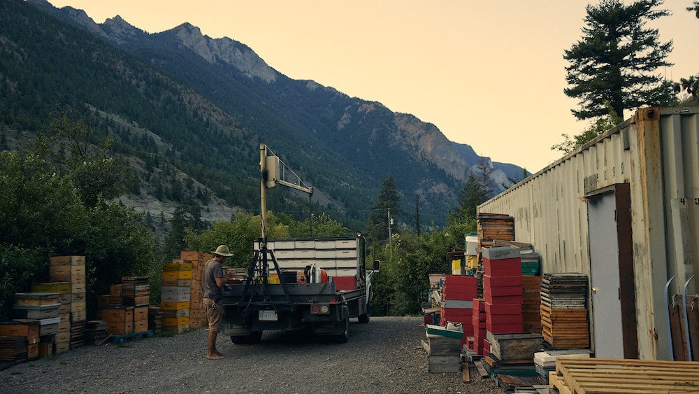 Image of beekeeper loading equipment onto truck outside of shipping container office, with stacks of hives, by Squamish, British Columbia-based portrait photographer Christian Tisdale. 