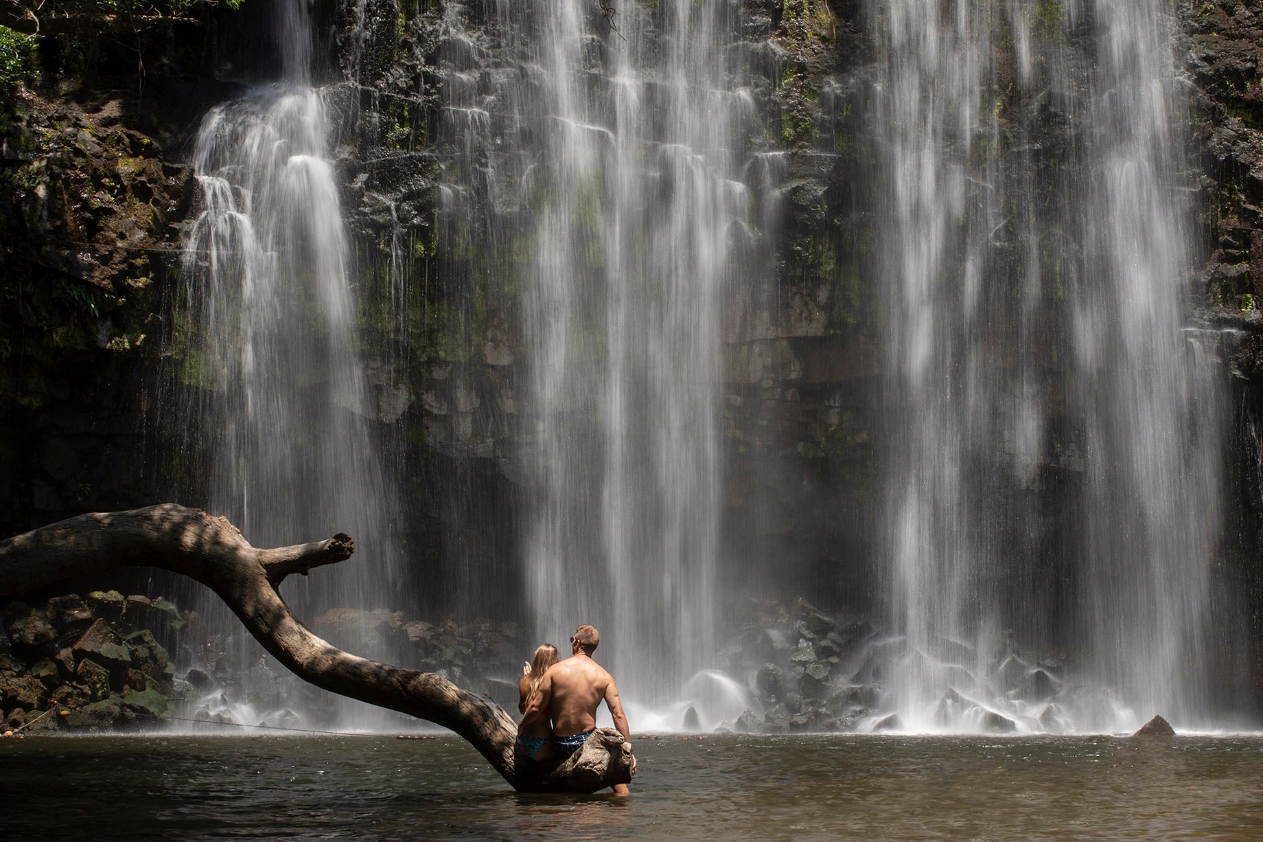 Two people sit underneath a waterfall in Costa Rican national park shot by Cristina Candel for Viajar 