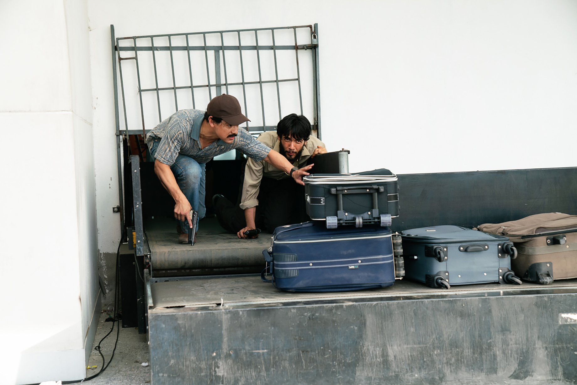 Two men climb through baggage claim at airport for Narcos: Mexico season 3 shot by Nicole Franco for Netflix