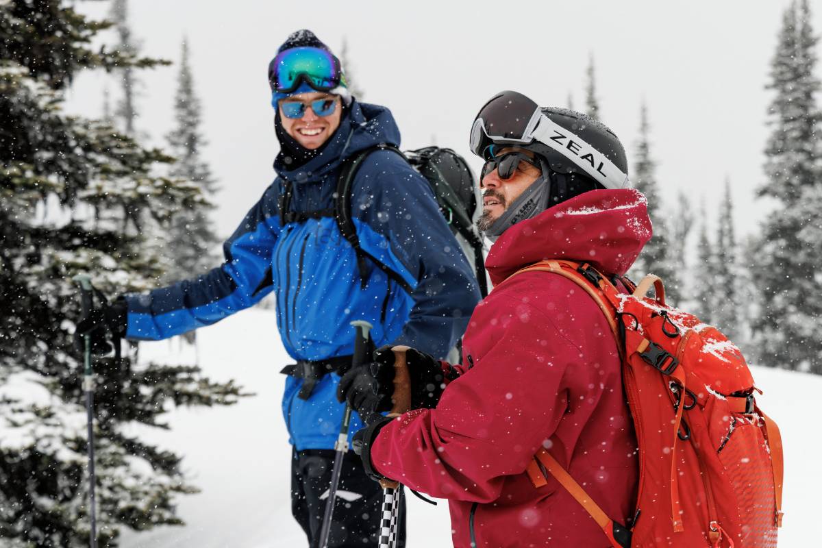 Photo of two snowboarders smiling as the snow falls around them.