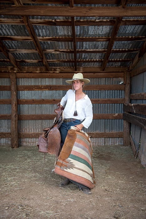Woman in barn carrying saddle wearing Ramblin Rose custom hat.