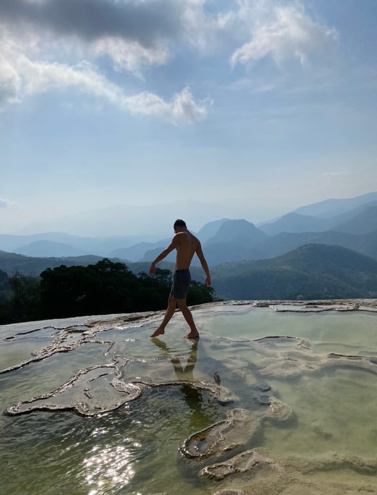 Figure walking in shallow textured natural pool before hazy mountain range.