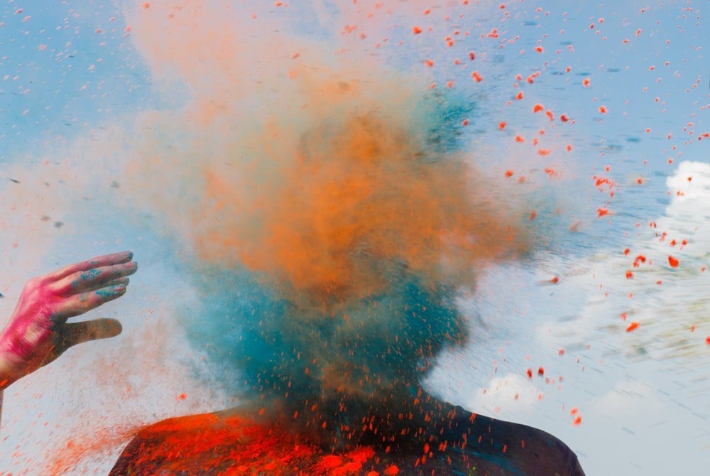 Photo of subject with face obscured by a cloud of colorful dust, second figure's throwing hand poised in release form to the side, by Mumbai-based portrait photographer Parikshit Rao.