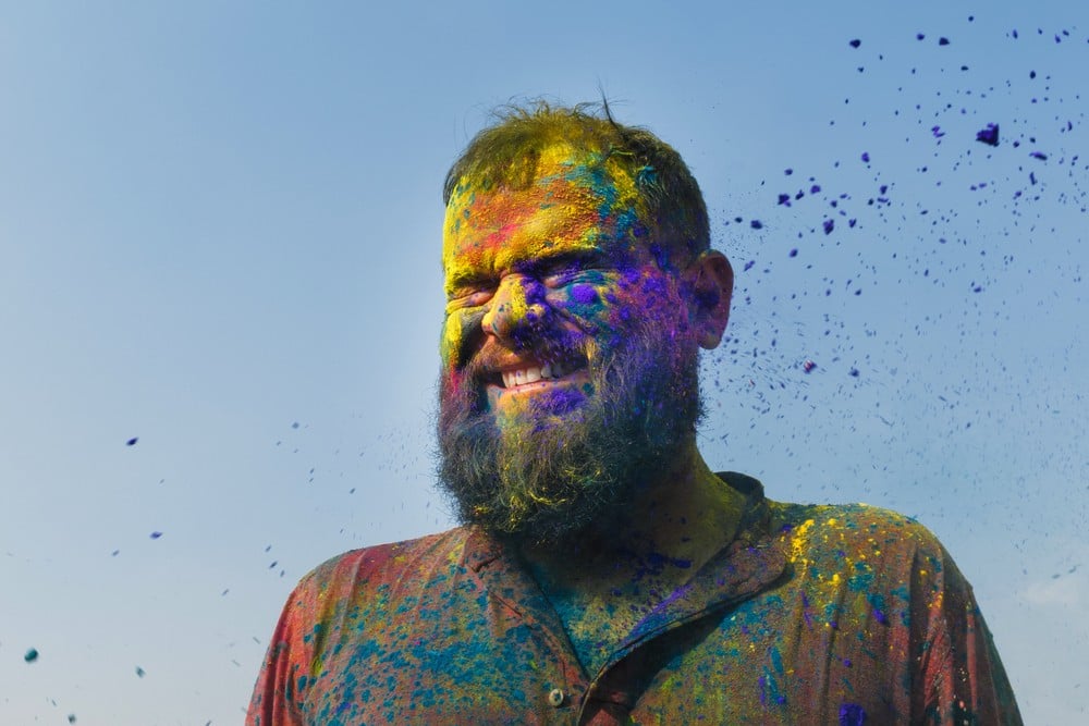 Imaged of bearded figure squinching face as color flies toward him, by Mumbai-based portrait photographer Parikshit Rao.