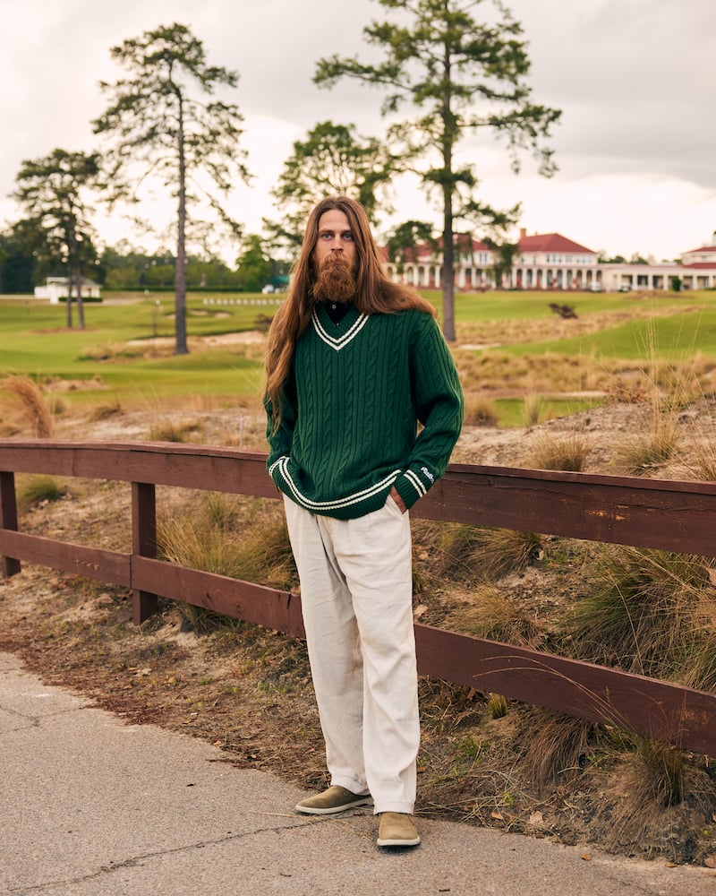 Image of long-haired bearded figure in green golf sweater in front of golf course clubhouse, by Charlotte, North Carolina-based fashion photographer Jackson Ray Petty.