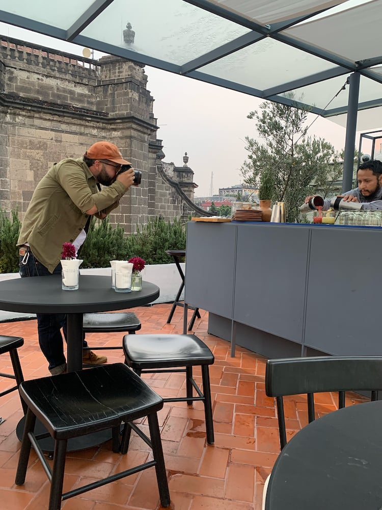 Behind-the-scenes photo of Andrew Reiner photographing a bartender pouring red and yellow drinks from two cocktail shakers.