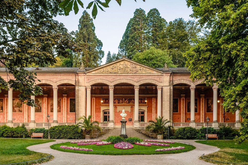 Exterior photo of grand terracotta colored building with columned archway and gardens, by Baden-Baden, Germany-based architecture photographer Torben Beeg.