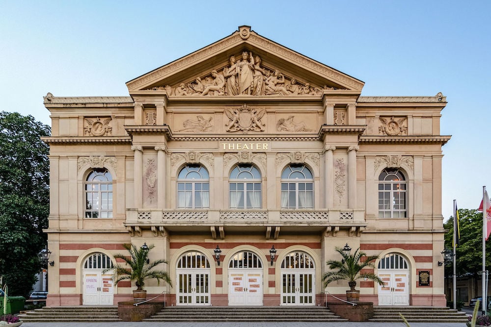 Exterior photo of historic beige stone theater, with ionic columns and statued arch by Baden-Baden, Germany-based architecture photographer Torben Beeg.