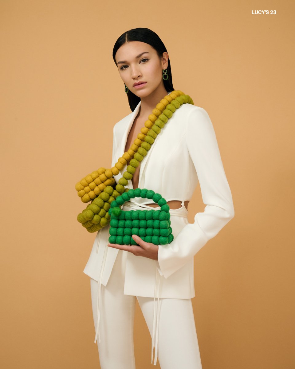 Photo by Matthew Mills of a model wearing three handbags, each a shade of green.