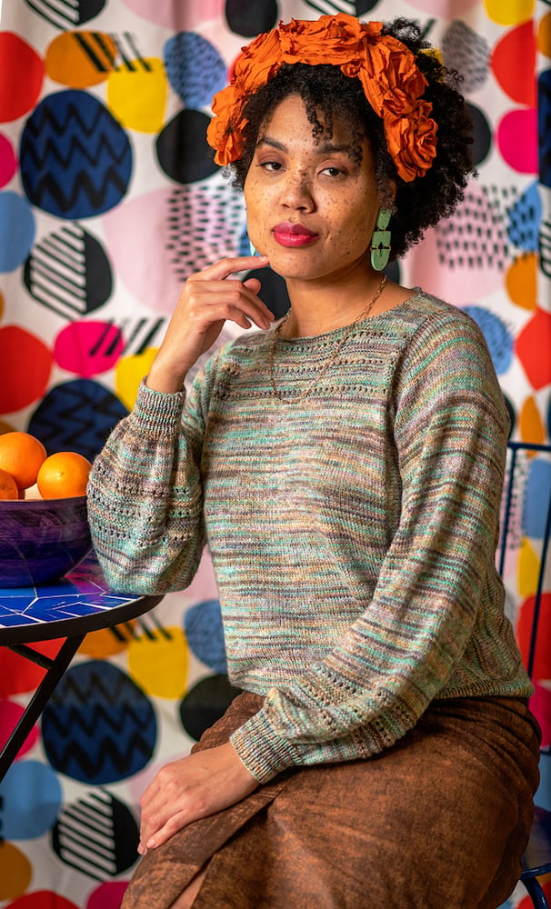 Image of talent with orange floral headwear and hand-knit pullover, sitting in front of colorful background with oranges, by Branford, Connecticut-based fashion photographer Gale Zucker. 