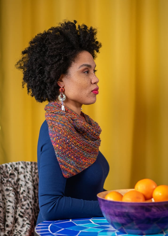 Profile of talent in folded hand-knit scarf, in blue sweater, in front of yellow curtain with bowl of oranges, by Branford, Connecticut-based fashion photographer Gale Zucker. 